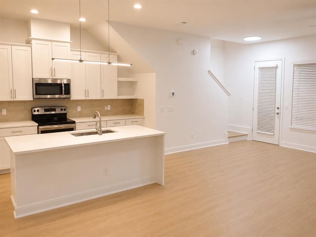 A modern kitchen features white cabinetry, a marble-topped island, and light wood-look flooring — 8543 PINTER STREET, ORLANDO, FL