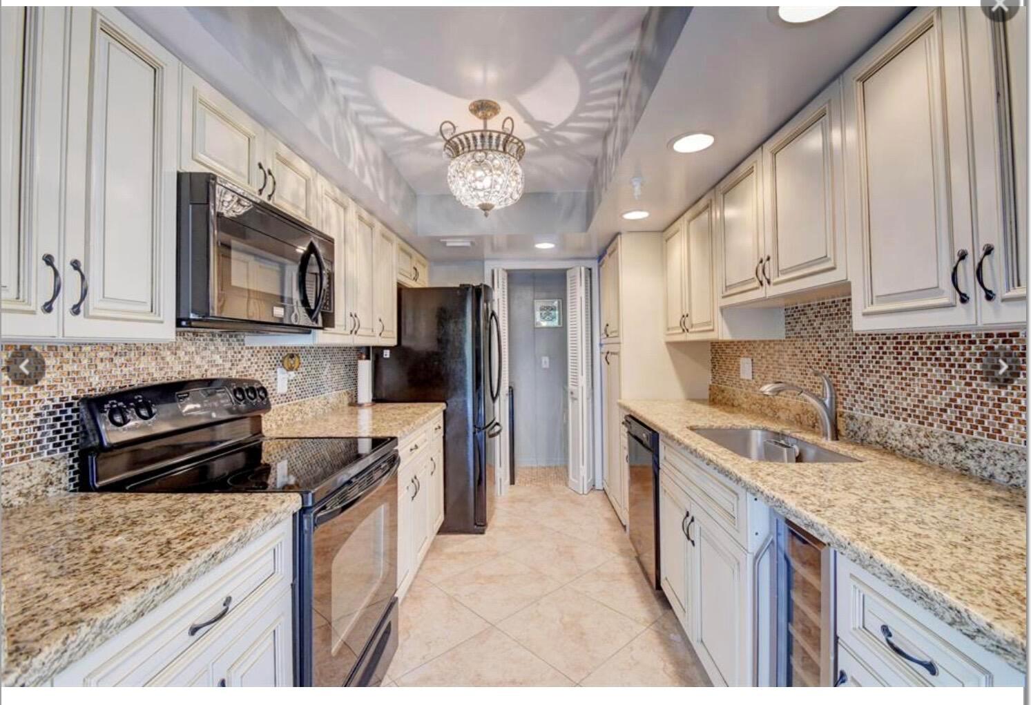 A galley kitchen features cream cabinets, granite countertops, a mosaic tile backsplash, and black appliances — 859 Jeffery Street # 3030, Boca Raton FL 33487, BOCA RATON, FL