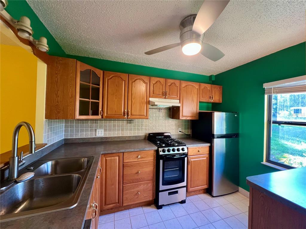 A kitchen features wood cabinets, stainless steel appliances, green walls, and a ceiling fan — 2971 MISSION DRIVE E UNIT 54F, CLEARWATER, FL