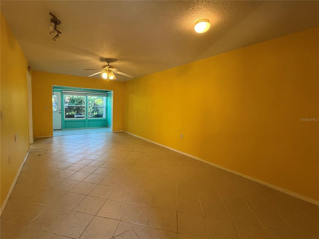 An empty room features yellow walls, light-colored tile flooring, a ceiling fan, and a window — 2971 MISSION DRIVE E UNIT 54F, CLEARWATER, FL