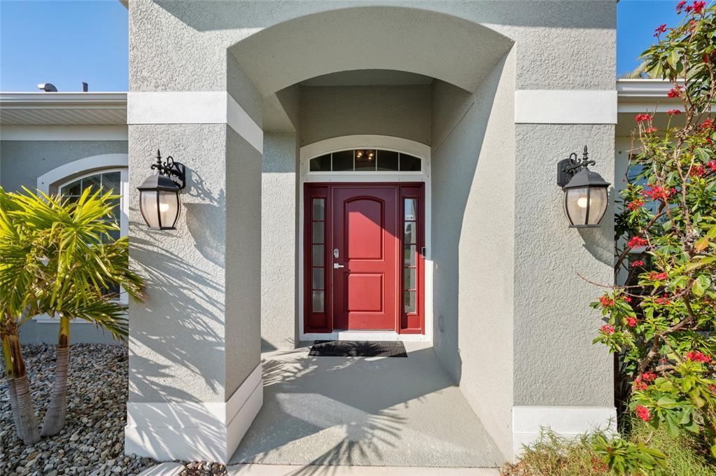A red front door with sidelights and an arched transom sits under a covered entryway — 17 WHITE MARSH LANE, ROTONDA WEST, FL