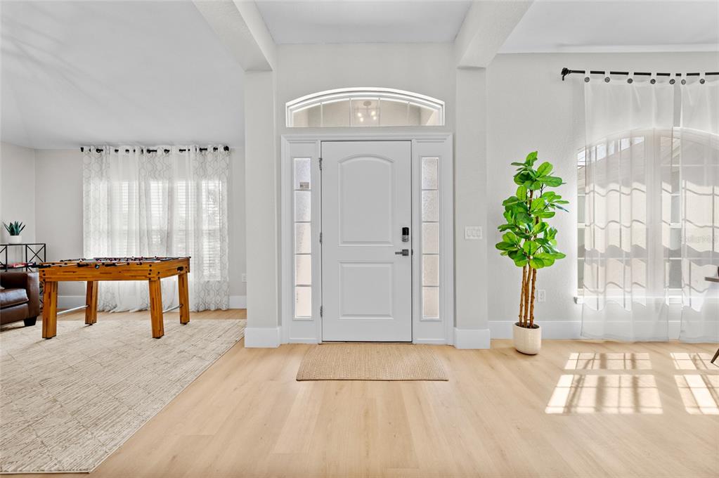 A bright entryway features light wood flooring, a white front door, and a foosball table — 17 WHITE MARSH LANE, ROTONDA WEST, FL