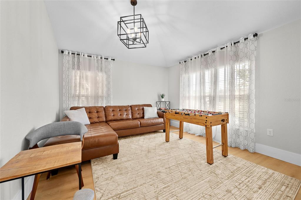 A living room features a brown leather sectional, a foosball table, and a geometric chandelier — 17 WHITE MARSH LANE, ROTONDA WEST, FL