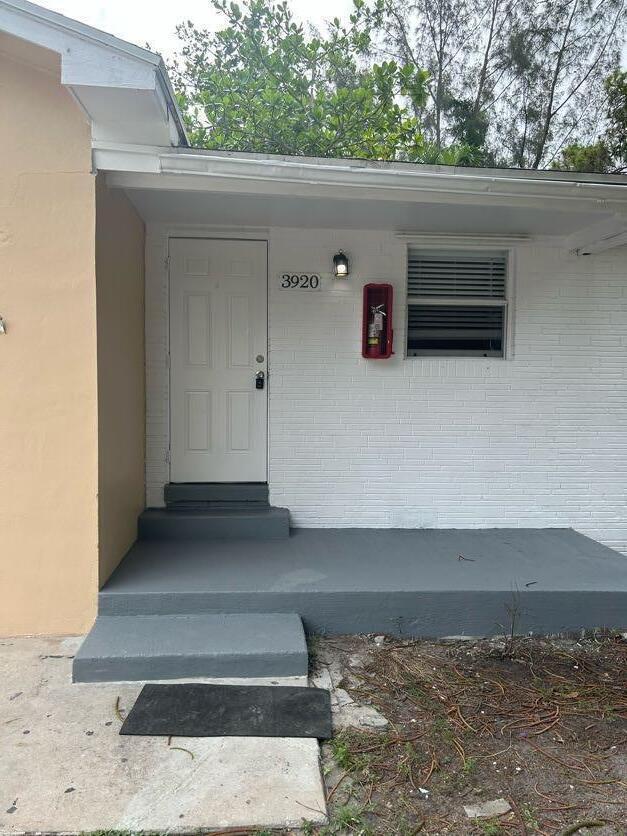 A white brick exterior features a front door, a window, and a wall-mounted fire extinguisher — 3920 7th Avenue N, FL 33461, FL