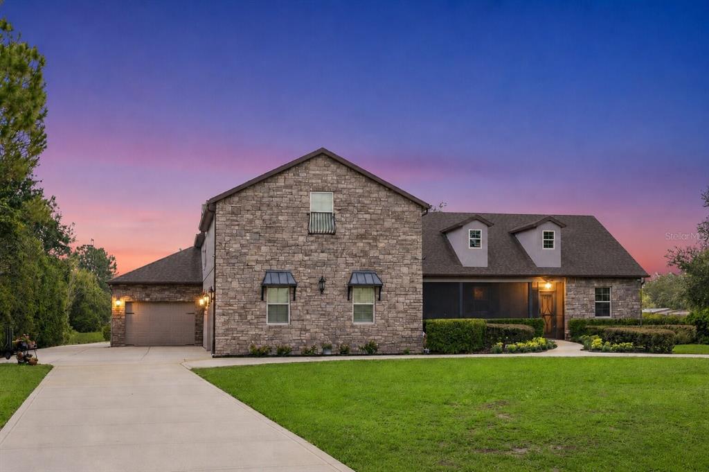 A two-story stone house with a garage and a screened-in porch at sunset — 2075 MUSTANG COURT, ST CLOUD, FL
