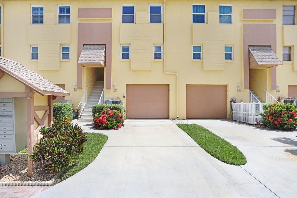A view of the exterior of a yellow multi-unit residential building with two garages — 314 WINDRUSH BOULEVARD UNIT 12, INDIAN ROCKS BEACH, FL