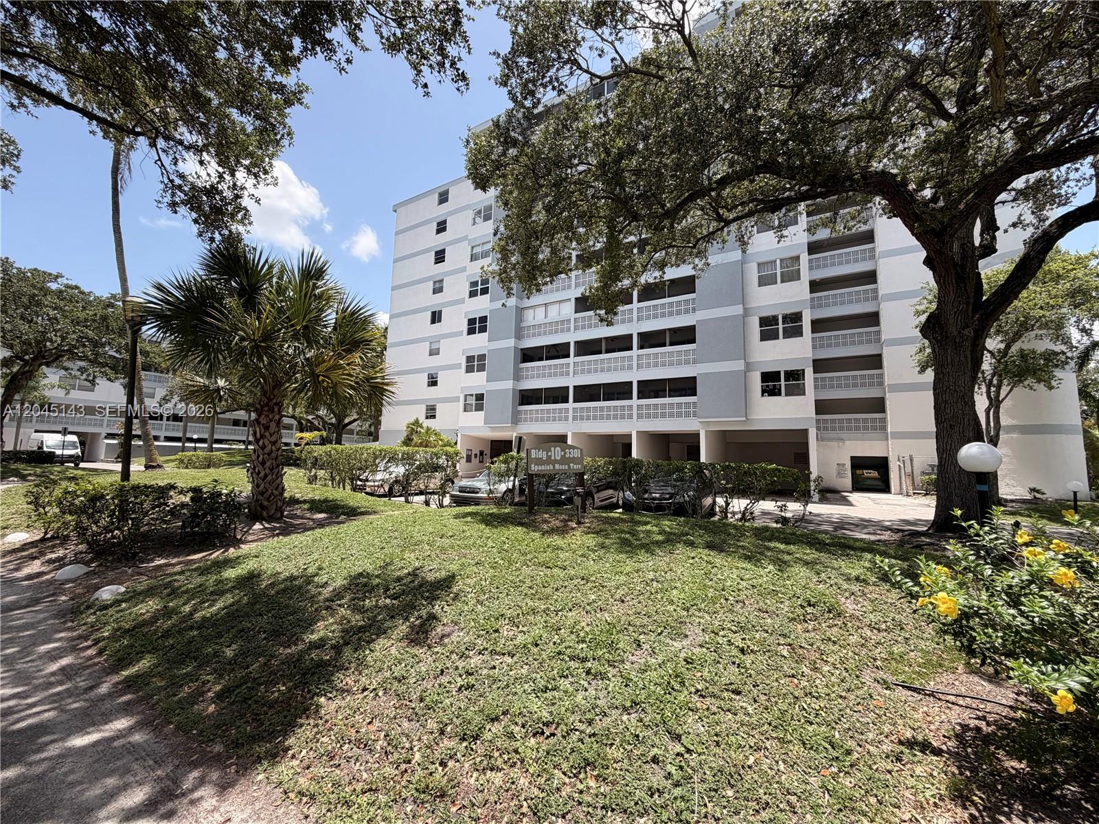 A multi-story residential building stands behind a grassy lawn with trees and parked cars — 3301 Spanish Moss Ter # 306, Lauderhill FL 33319, LAUDERHILL, FL