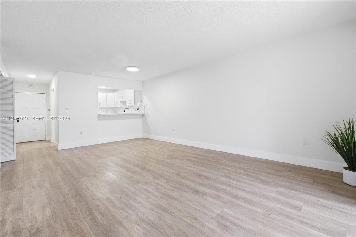 An empty living room features light wood-look flooring, white walls, and an open kitchen pass-through — 6960 Miami Gardens Dr # 124, Hialeah FL 33015, HIALEAH, FL