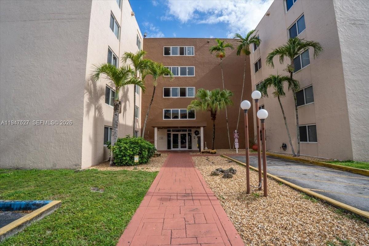 A red brick walkway leads to the entrance of a multi-story tan apartment building — 6960 Miami Gardens Dr # 124, Hialeah FL 33015, HIALEAH, FL