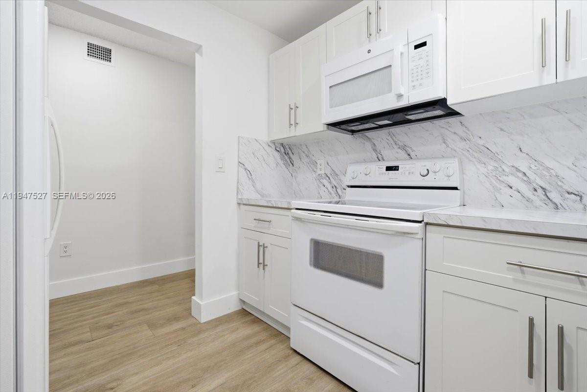 A white kitchen features marble-patterned backsplashes, white cabinetry, and light wood-look flooring — 6960 Miami Gardens Dr # 124, Hialeah FL 33015, HIALEAH, FL