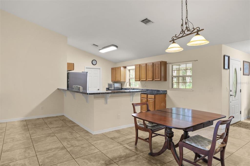 A kitchen with wood cabinets, a breakfast bar, and tile flooring opens to a dining area — 35819 NOVA LANE, EUSTIS, FL