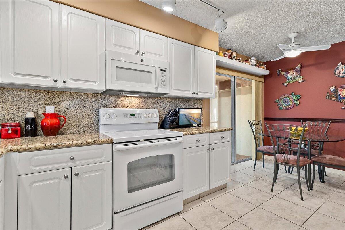 A kitchen features white cabinets, granite countertops, a white stove, and a dining area — 9927 Seacrest Circle # 102, Boynton Beach FL 33437, BOYNTON BEACH, FL