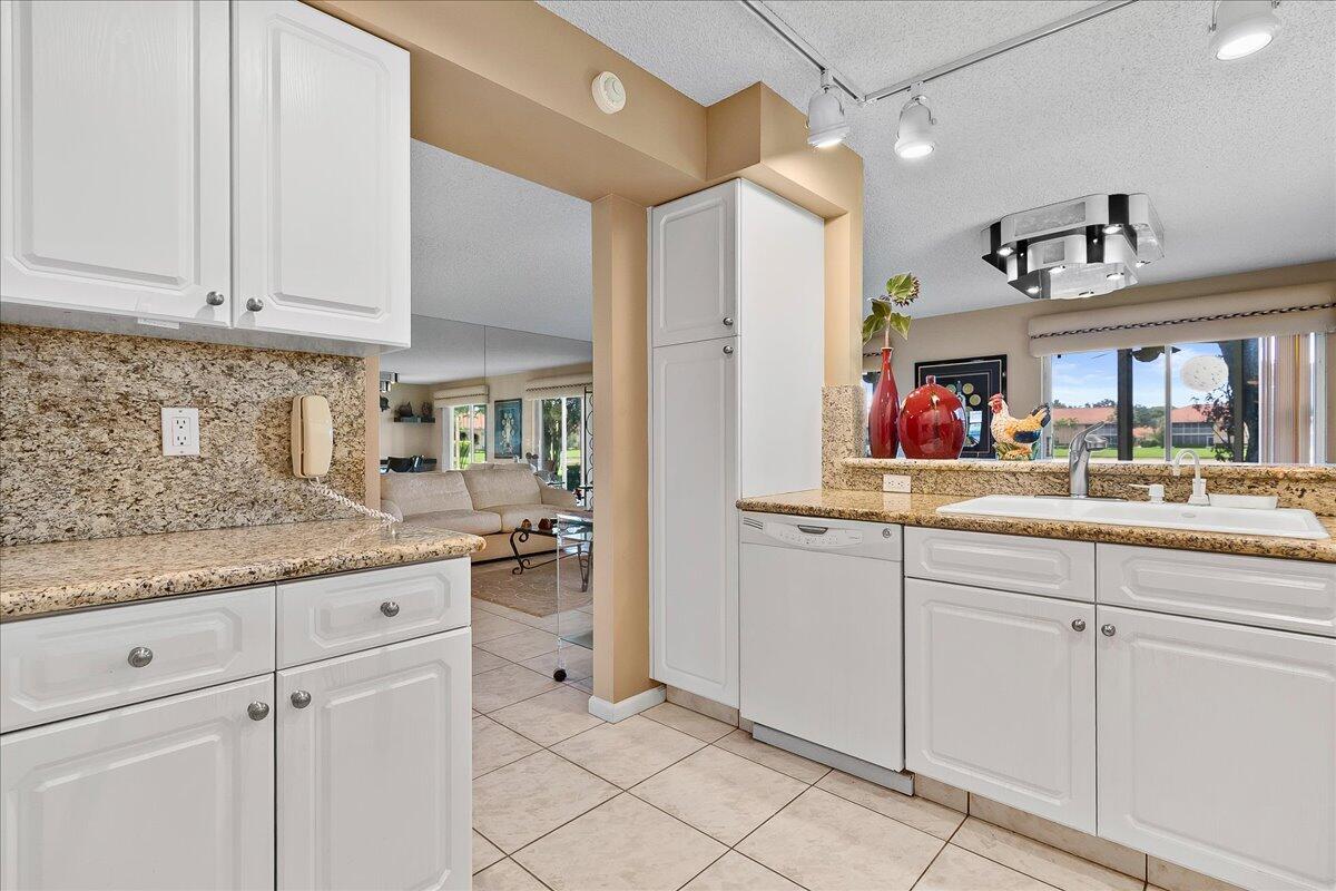 A kitchen with white cabinets, granite countertops, and a view into the adjacent living room — 9927 Seacrest Circle # 102, Boynton Beach FL 33437, BOYNTON BEACH, FL