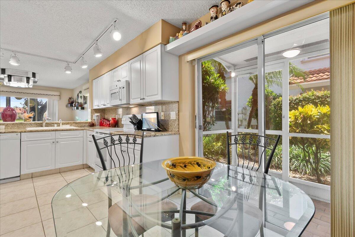 A kitchen and dining area with white cabinets, granite countertops, and a glass sliding door — 9927 Seacrest Circle # 102, Boynton Beach FL 33437, BOYNTON BEACH, FL