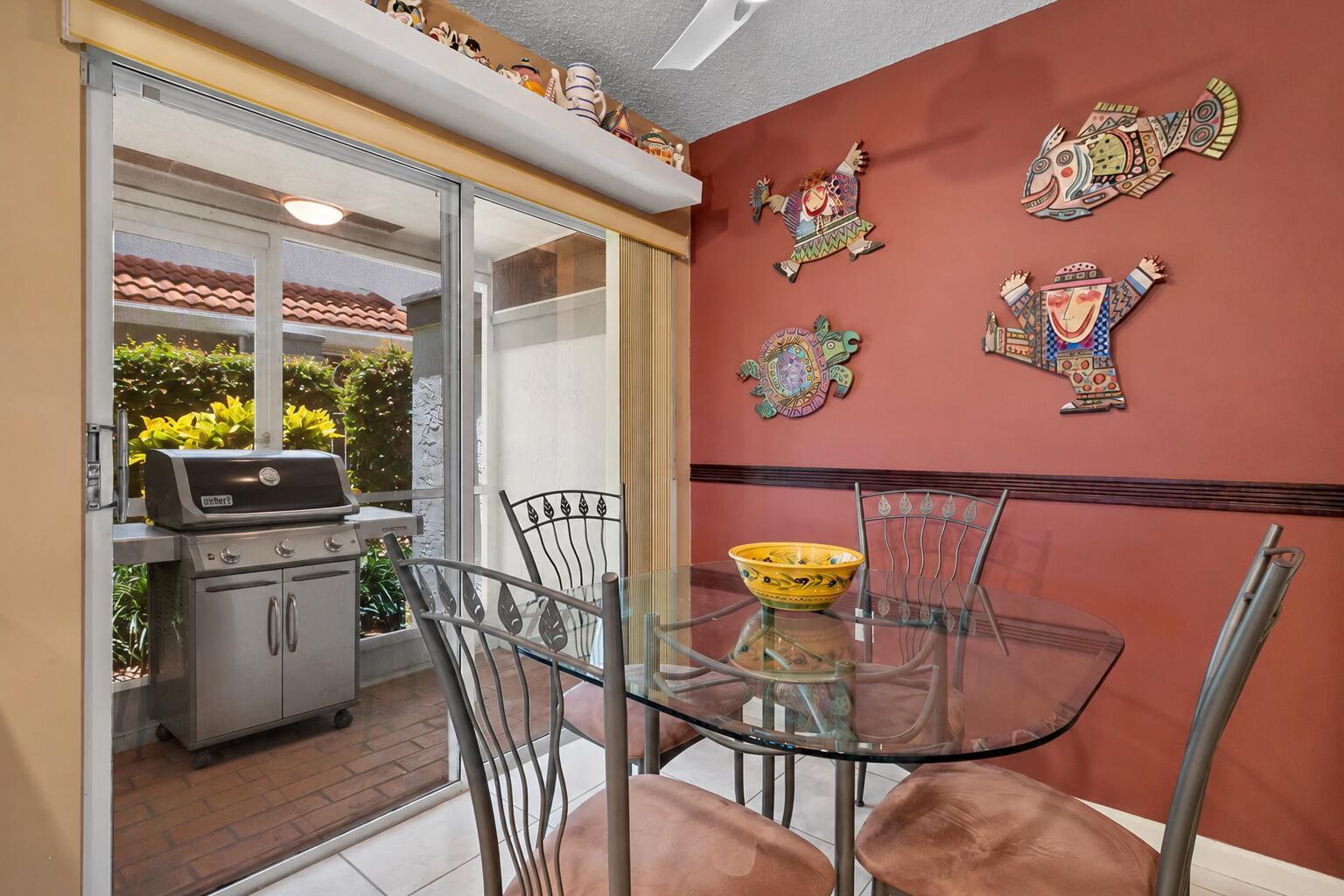 A dining room with a glass table, metal chairs, and colorful wall art near a patio — 9927 Seacrest Circle # 102, Boynton Beach FL 33437, BOYNTON BEACH, FL