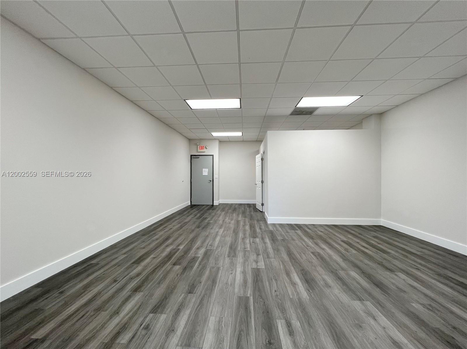 An empty office space features gray wood-look flooring, white walls, and a drop ceiling — 7791 NW 46th St # 104, Doral FL 33166, DORAL, FL