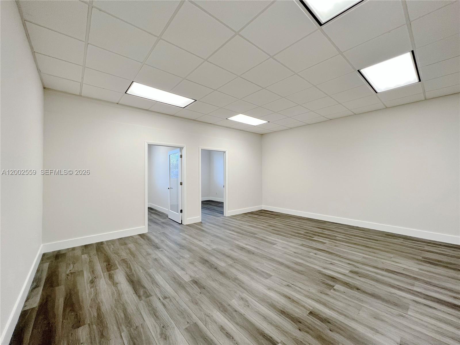 An empty office room features white walls, a drop ceiling, and wood-look vinyl flooring — 7791 NW 46th St # 104, Doral FL 33166, DORAL, FL