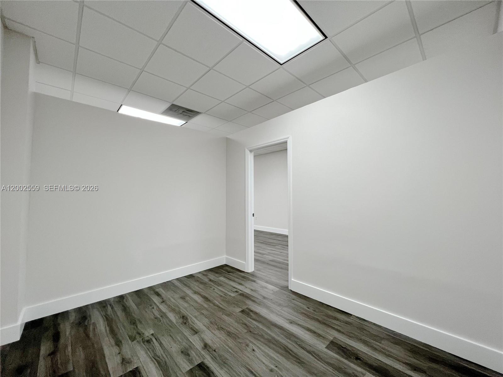 An empty office space features white walls, a drop ceiling, and wood-look flooring — 7791 NW 46th St # 104, Doral FL 33166, DORAL, FL