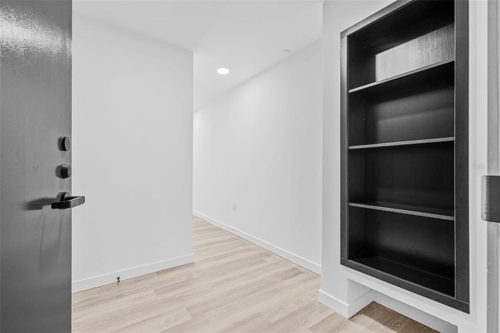 A hallway with light wood flooring features a built-in black shelving unit on the right — 221 MAIN STREET N UNIT A3-1506, ST PETERSBURG, FL