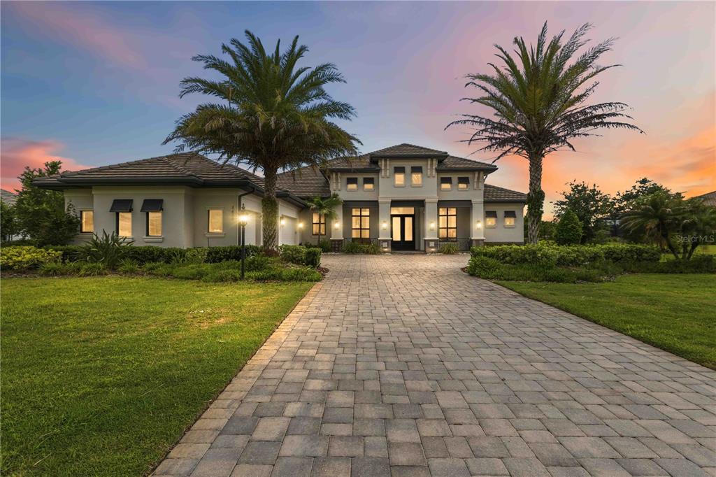 A two-story house with a paved driveway, palm trees, and a sunset sky — 8452 LINDRICK LANE, BRADENTON, FL