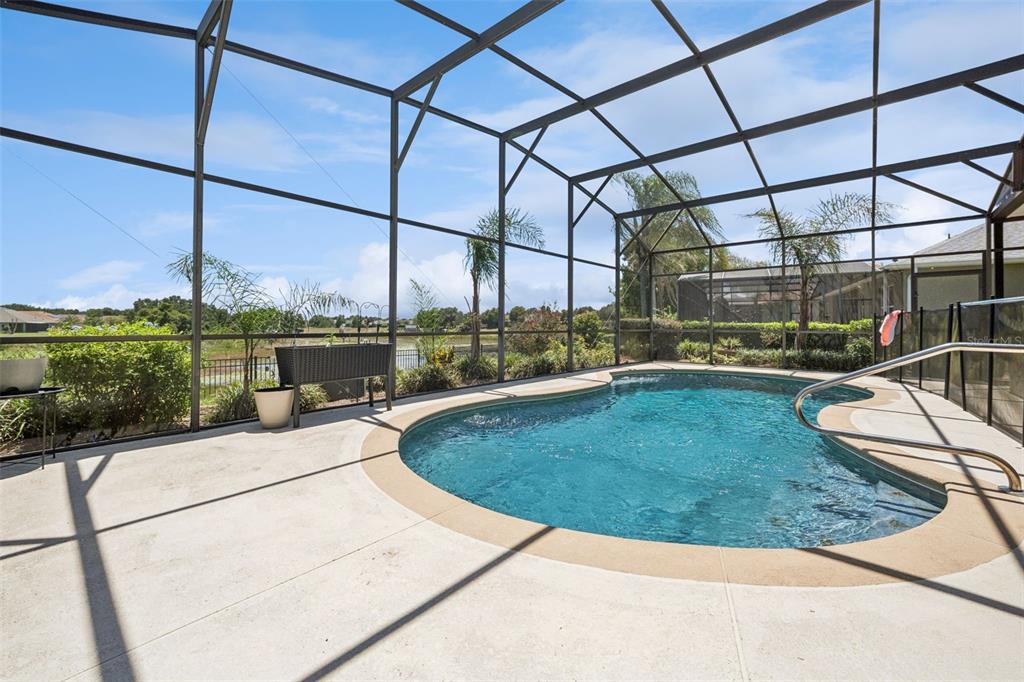 A screened-in patio features a kidney-shaped swimming pool overlooking a grassy landscape and pond — 220 BAYOU BEND ROAD, GROVELAND, FL