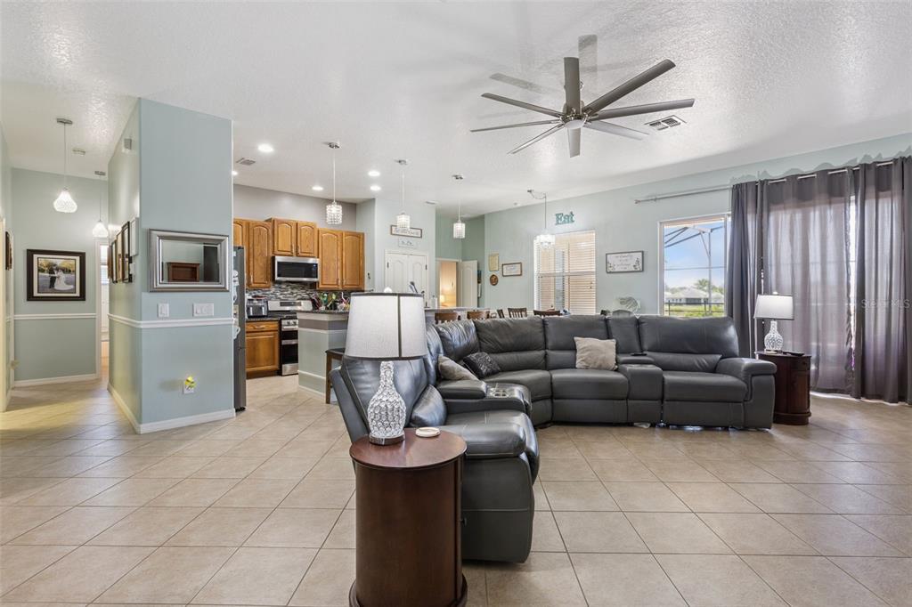An open-concept living room features a large gray sectional, tile flooring, and an adjacent kitchen — 220 BAYOU BEND ROAD, GROVELAND, FL