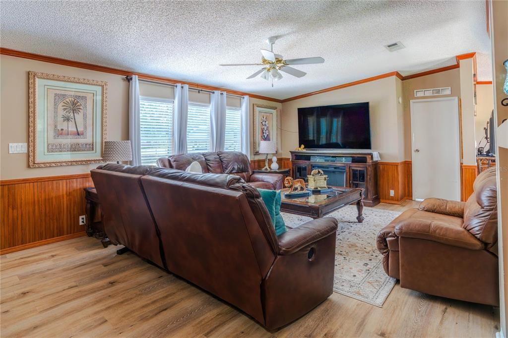 A living room features wood-paneled walls, leather furniture, a large television, and light wood flooring — 4100 MARION COUNTY ROAD, WEIRSDALE, FL