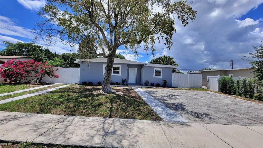 A single-story blue house features a paved driveway, a large tree, and white fencing — 266 NE 42nd Street, Deerfield Beach FL 33064, DEERFIELD BEACH, FL