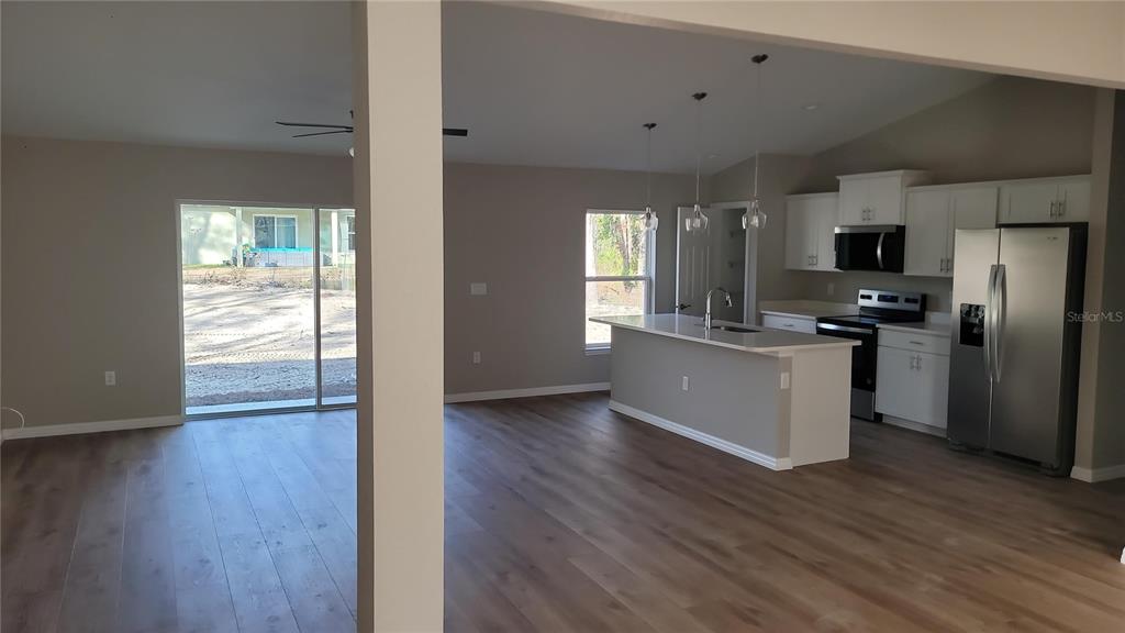 An open-concept kitchen and living area features light wood flooring, white cabinetry, and stainless appliances — 5982 N MATHESON DRIVE, CITRUS SPRINGS, FL