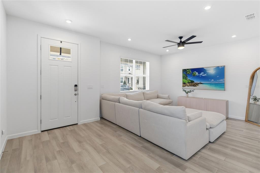 A living room features light wood-look flooring, a white sectional sofa, and a wall-mounted television — 1326 TARFLOWER DRIVE, WINTER SPRINGS, FL