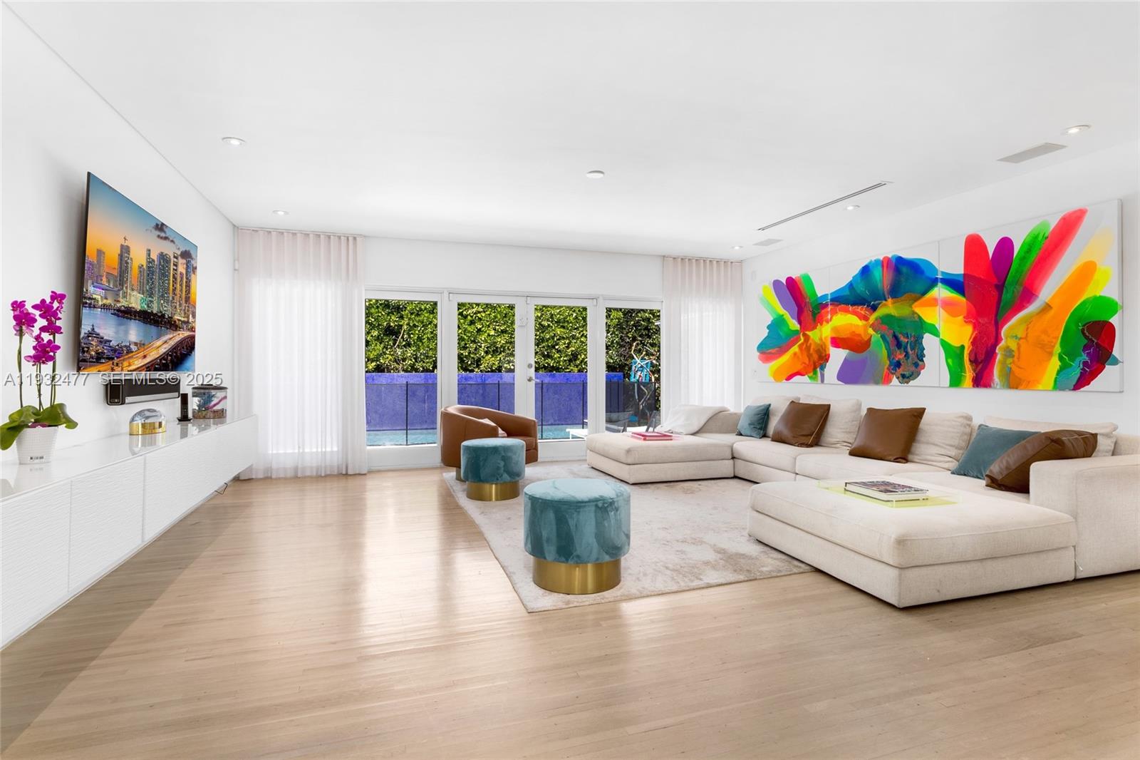 A modern living room features a large sectional sofa, colorful wall art, and glass doors — 6420 Pinetree Drive Cir, Miami Beach FL 33141, MIAMI BEACH, FL