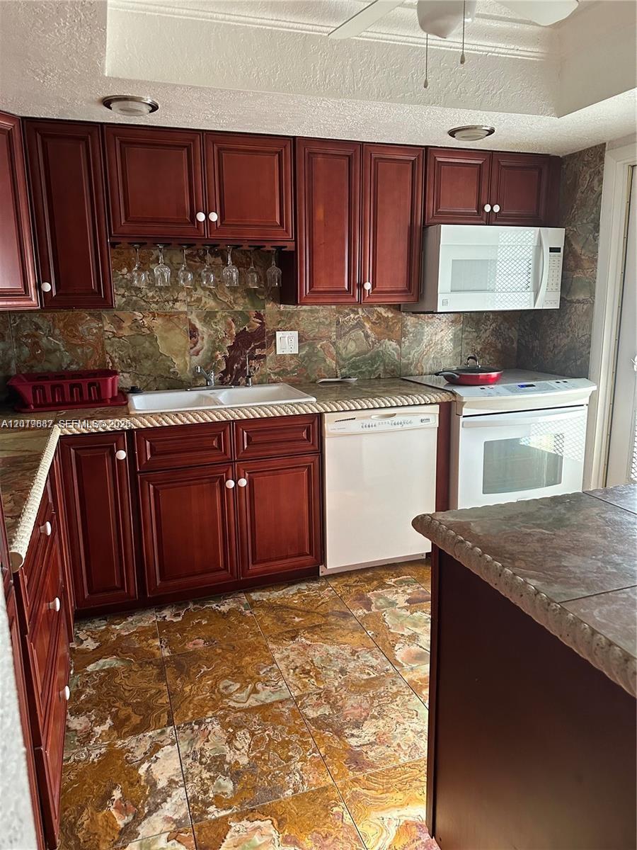 A kitchen features cherry wood cabinets, a white dishwasher, and patterned stone tile flooring — 19051 NE 2nd Ave # 1514, Miami FL 33179, MIAMI, FL