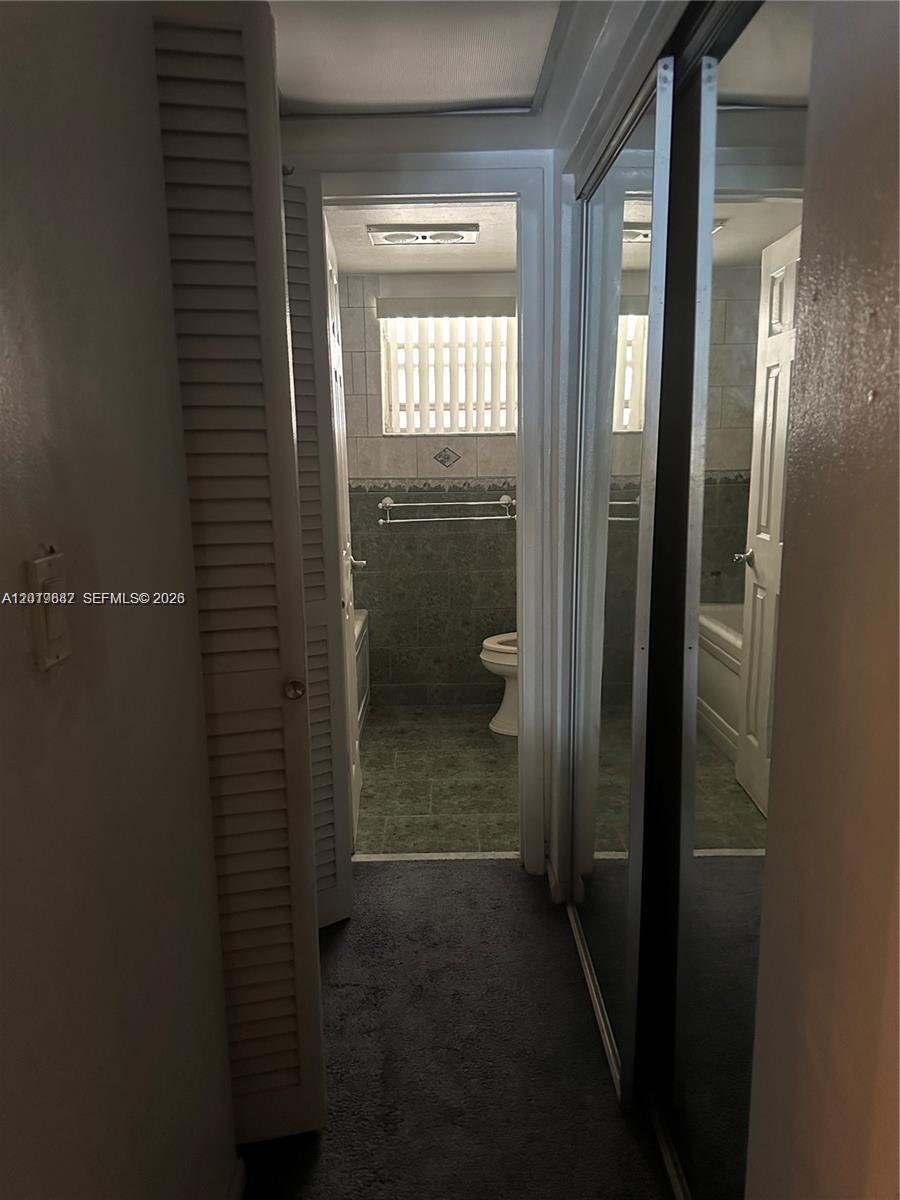 A carpeted hallway leads to a bathroom featuring tiled walls, a toilet, and a tub — 19051 NE 2nd Ave # 1514, Miami FL 33179, MIAMI, FL