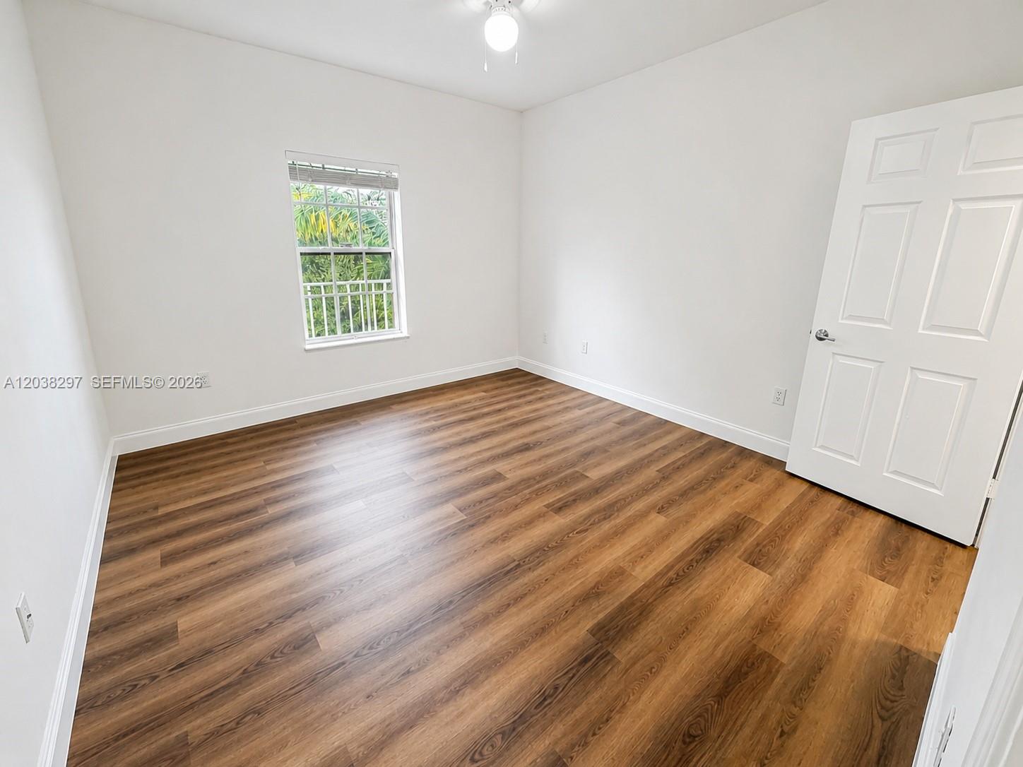 An empty bedroom features white walls, wood-look flooring, a ceiling fan, and a window — 7000 SW 80th St # 401, Miami FL 33143, MIAMI, FL