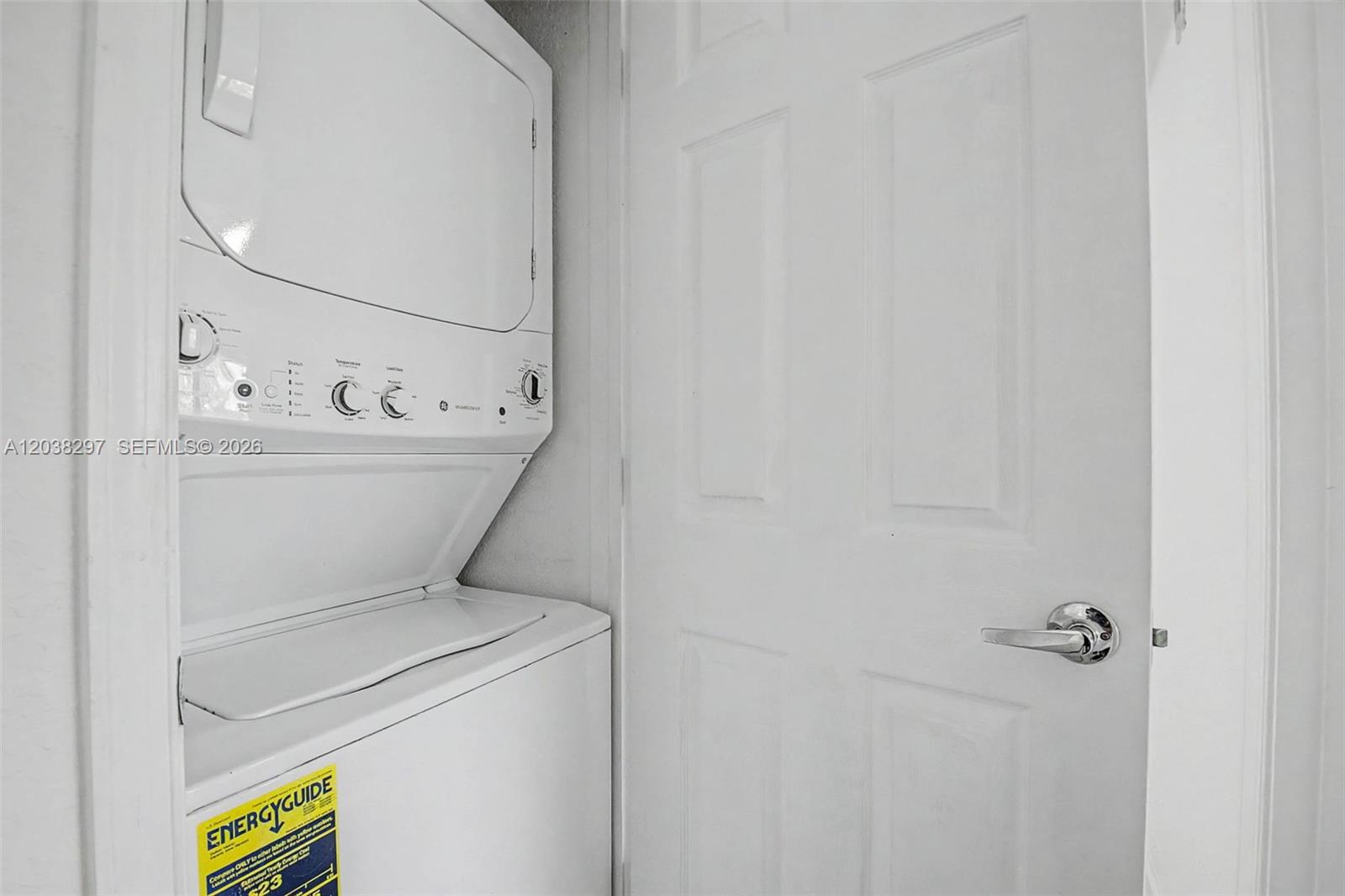 A stacked washer and dryer unit sits next to a white door in a laundry closet — 7000 SW 80th St # 401, Miami FL 33143, MIAMI, FL