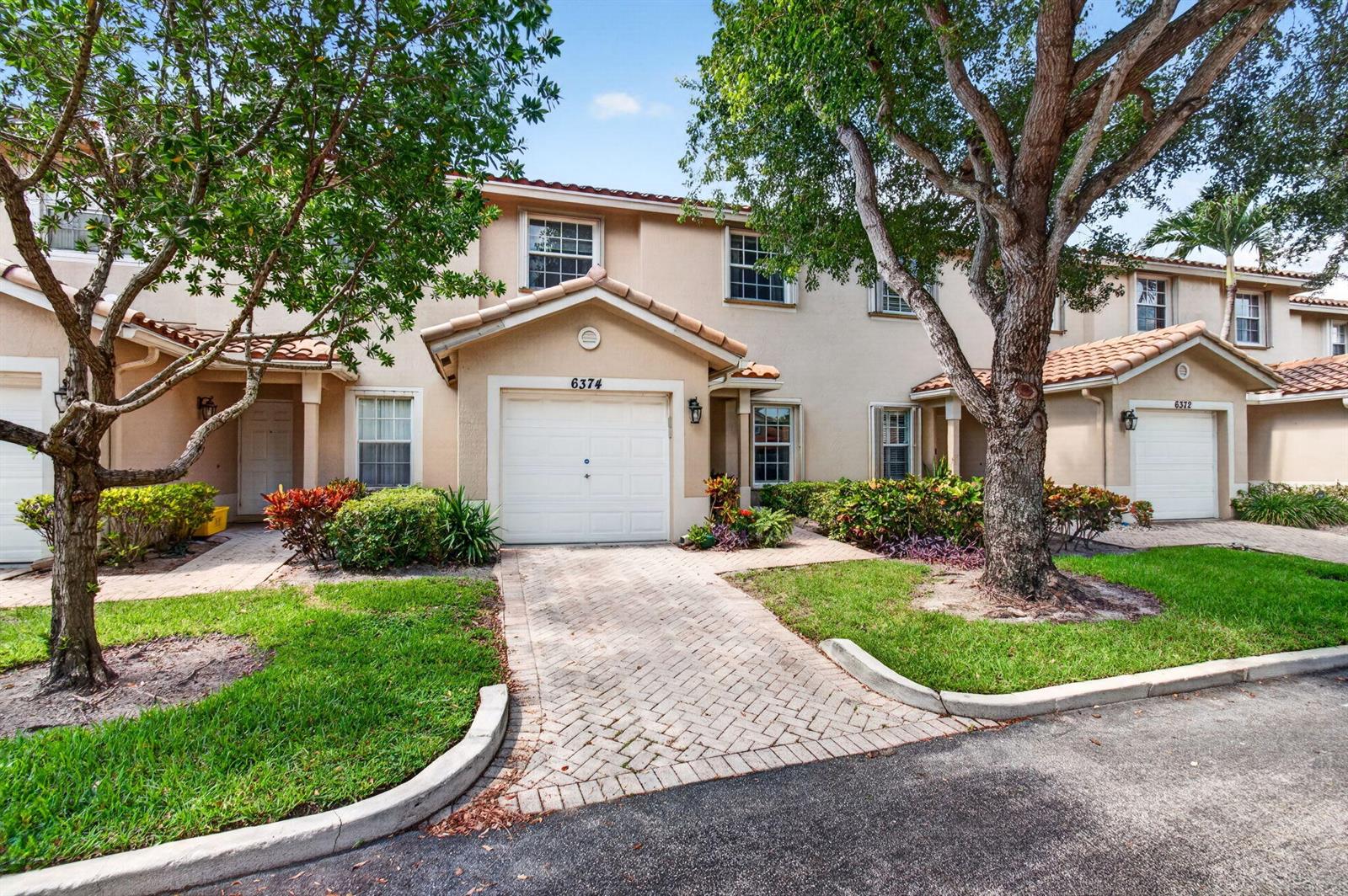 A two-story townhouse with a beige stucco facade, a garage, and a brick paver driveway — 6374 Park Lake Circle, Boynton Beach FL 33437, BOYNTON BEACH, FL