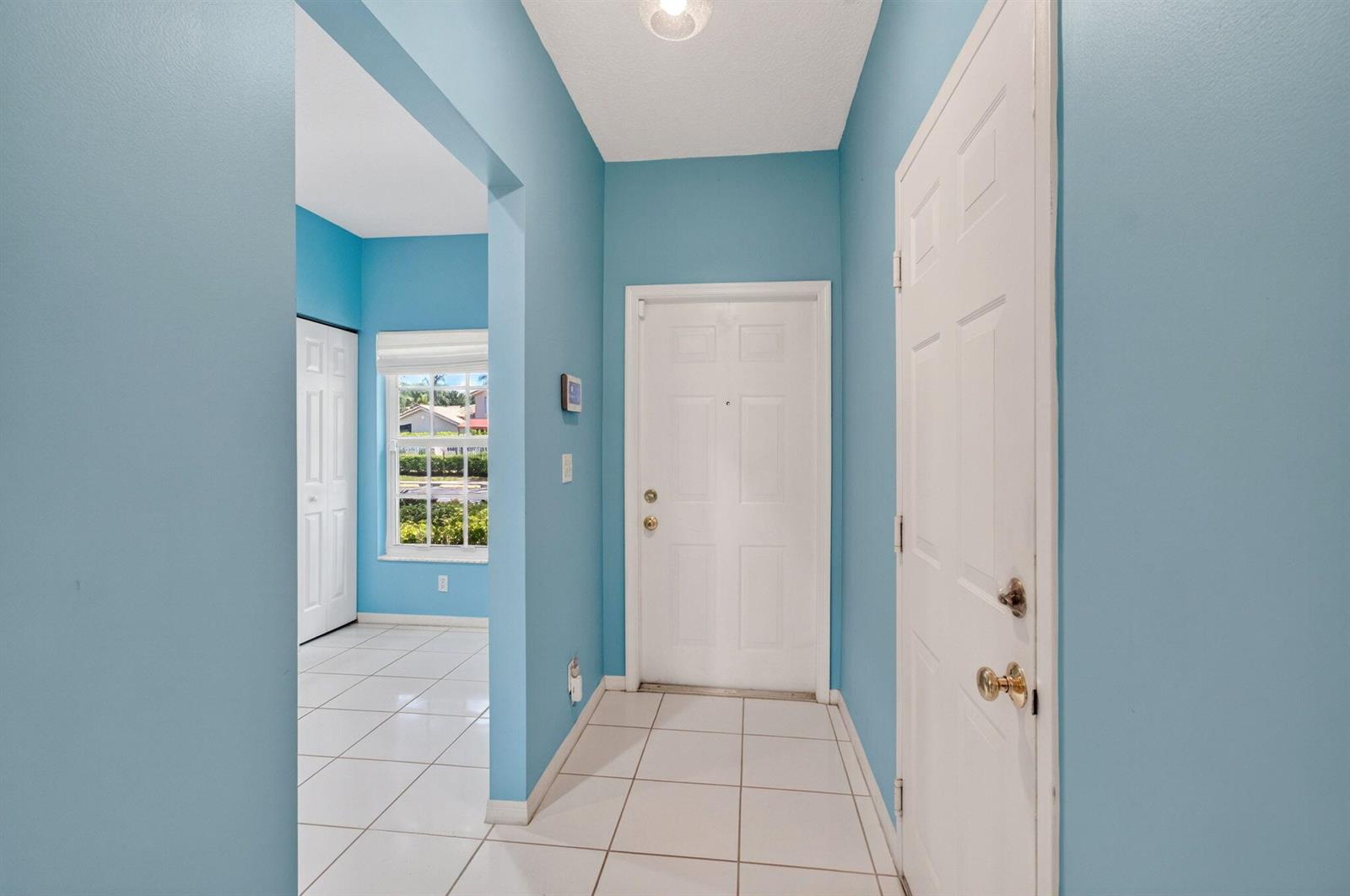 An entryway with light blue walls, white tile flooring, and two white doors — 6374 Park Lake Circle, Boynton Beach FL 33437, BOYNTON BEACH, FL