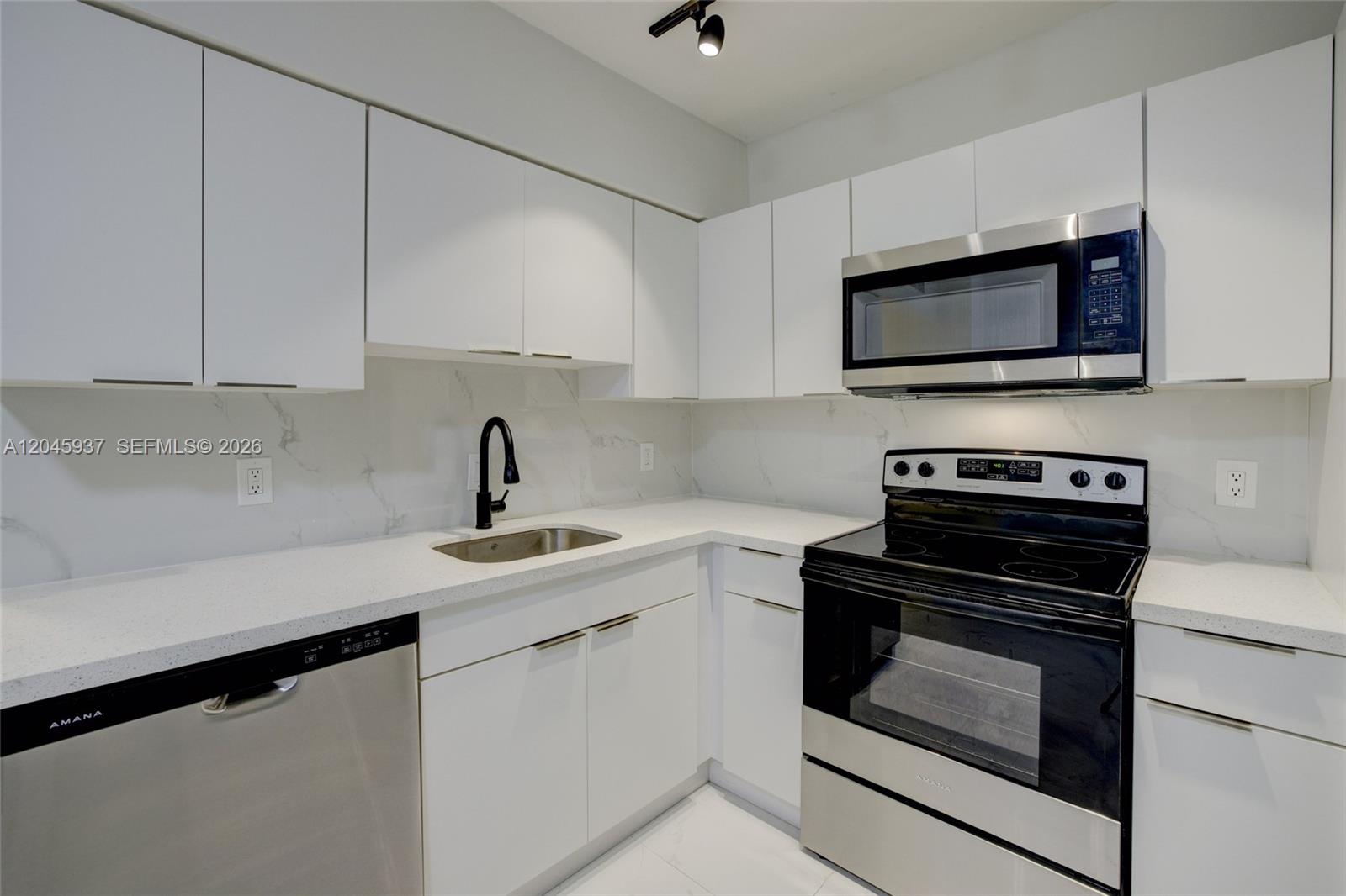 A modern kitchen features white cabinets, stainless steel appliances, and a marble-patterned backsplash — 1740 Funston ST # 6, Hollywood FL 33020, HOLLYWOOD, FL