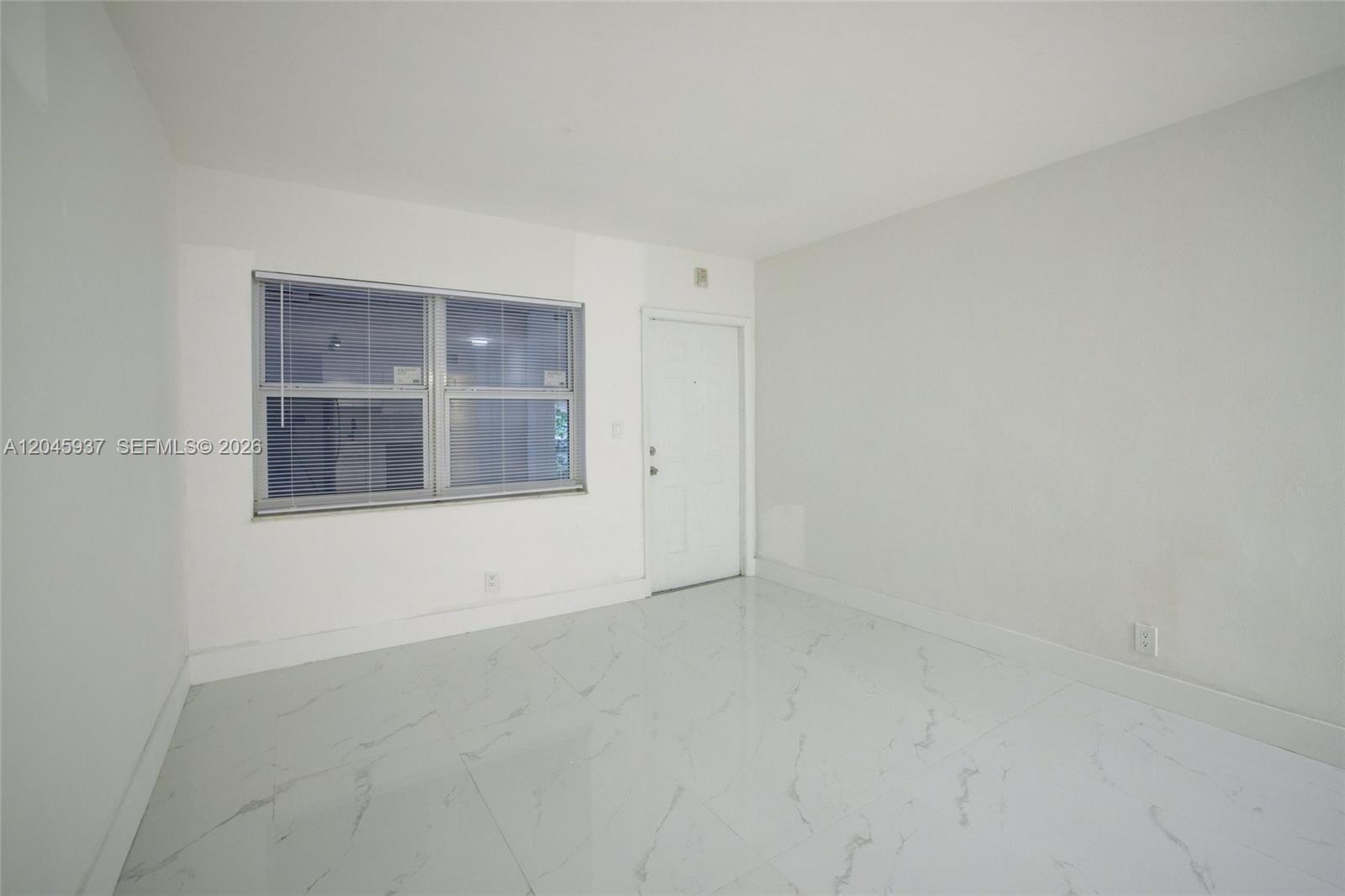 An empty room features white walls, white marble-patterned tile flooring, and a single window — 1740 Funston ST # 6, Hollywood FL 33020, HOLLYWOOD, FL