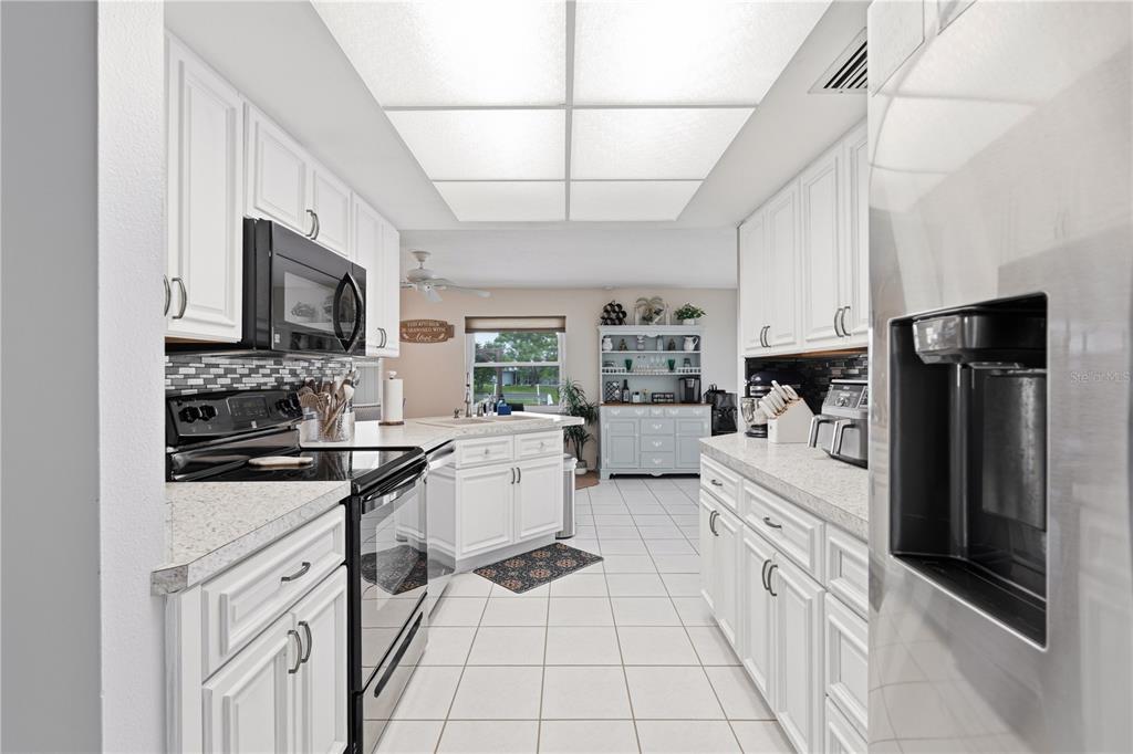 A white kitchen features a central island, stainless steel appliances, and a tiled floor — 2284 BROAD RANCH DRIVE, PORT CHARLOTTE, FL