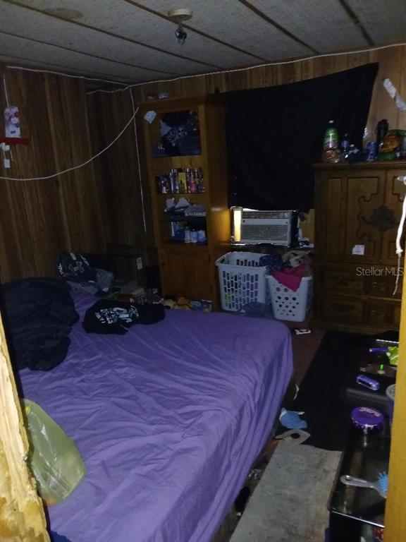 A bedroom features wood-paneled walls, a purple bedspread, a tall wooden bookshelf, and laundry baskets — 14847 SE 47TH COURT, SUMMERFIELD, FL