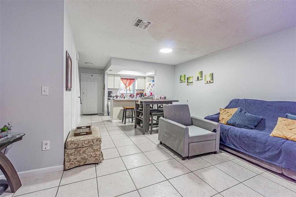 A living room with tile flooring, a blue sofa, a gray armchair, and an open kitchen — 4010 OAK LIMB COURT, TAMPA, FL