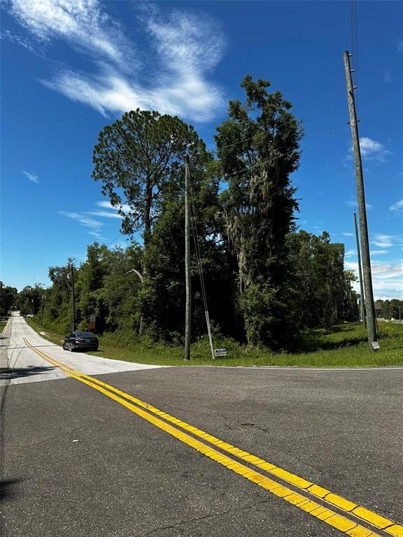 A paved road intersection leads to a wooded lot with utility poles and a parked car — xx THRASHER DR, BRONSON, FL