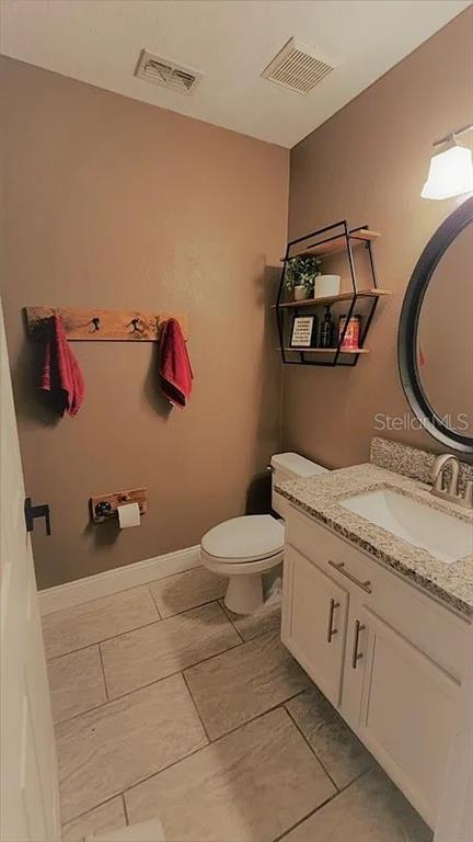 A bathroom features a white vanity with granite countertop, a toilet, and wall-mounted shelving — 254 BRIDGE CREEK BOULEVARD, OCOEE, FL
