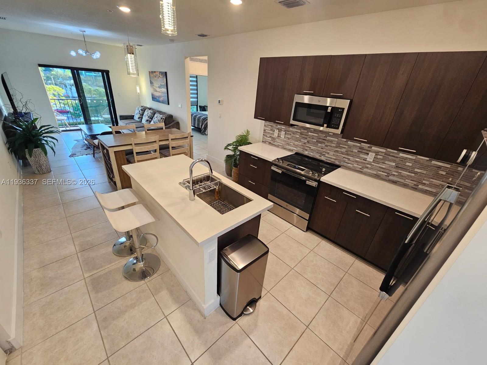 A modern kitchen with dark wood cabinets, white countertops, and an island with bar seating — 8301 NW 41st St # 402, Doral FL 33166, DORAL, FL
