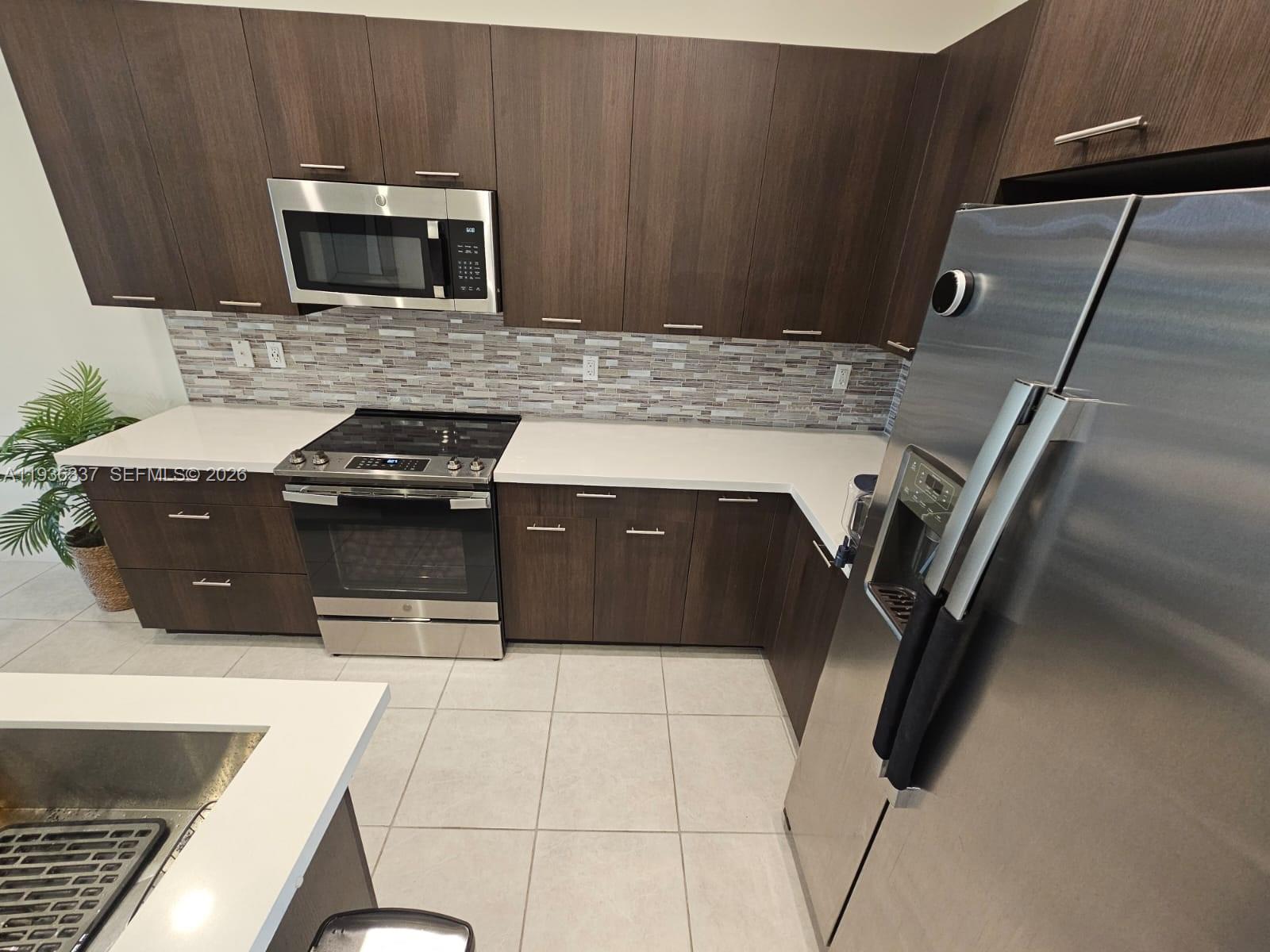 A kitchen features dark wood cabinets, stainless steel appliances, white countertops, and a tiled backsplash — 8301 NW 41st St # 402, Doral FL 33166, DORAL, FL