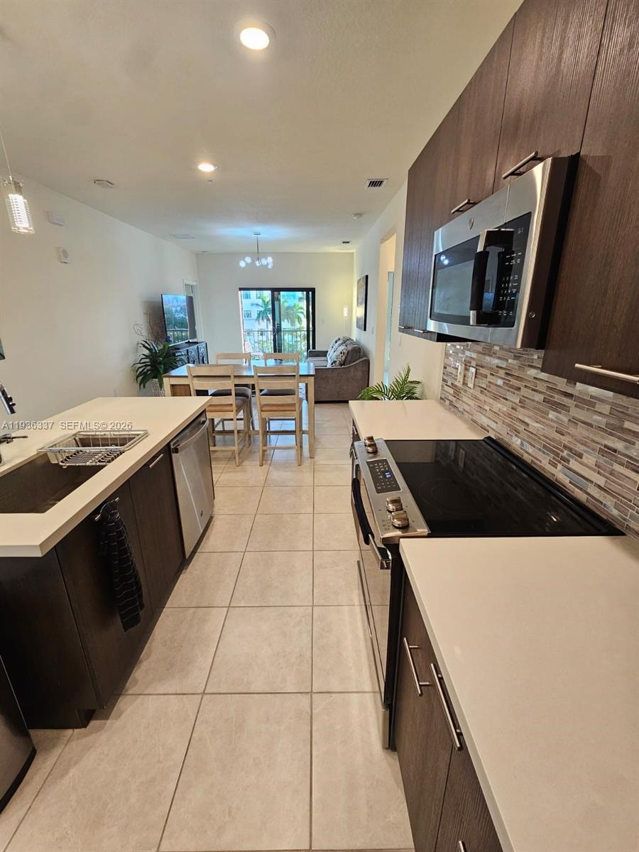 A modern kitchen with dark cabinetry and stainless steel appliances opens into a dining area — 8301 NW 41st St # 402, Doral FL 33166, DORAL, FL