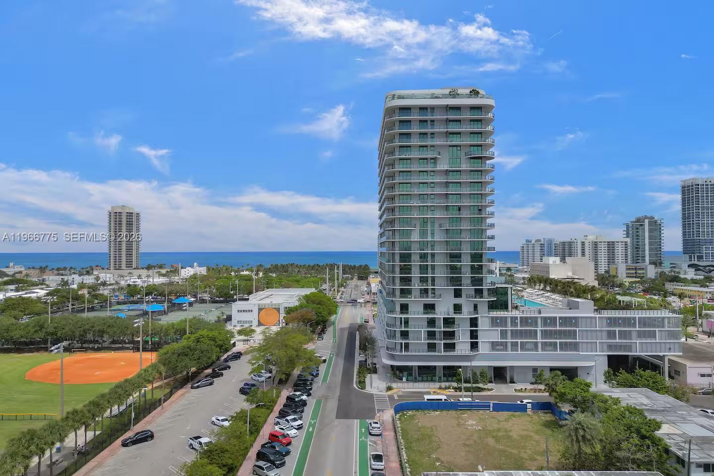 An aerial view shows a modern high-rise building next to a street and park — 580 72nd St # 705, Miami Beach FL 33141, MIAMI BEACH, FL