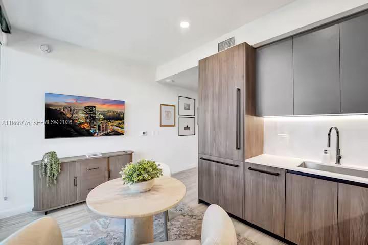 A modern kitchen and dining area features wood-toned cabinetry, a round table, and wall-mounted television — 580 72nd St # 705, Miami Beach FL 33141, MIAMI BEACH, FL