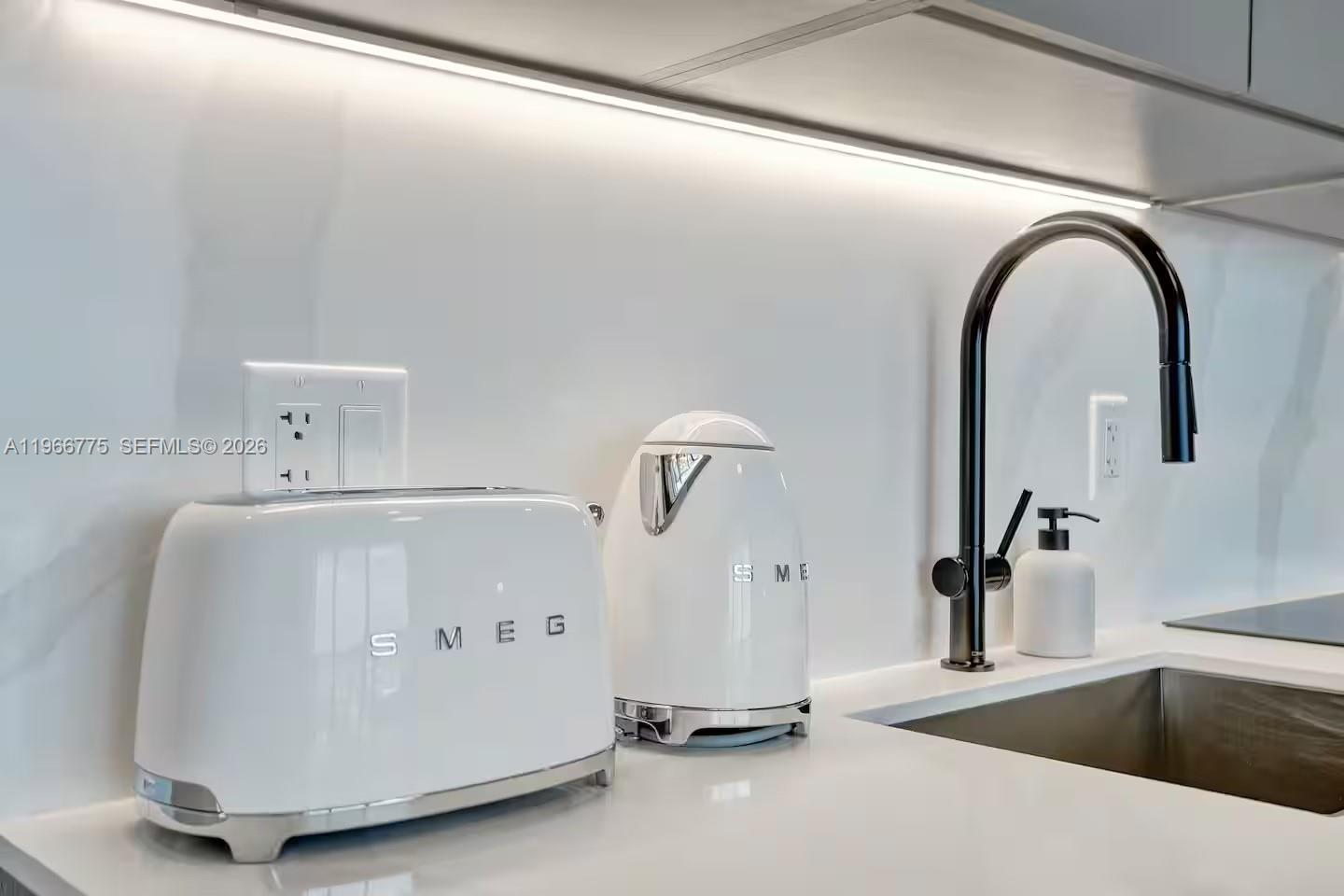 A white kitchen counter features a Smeg toaster, kettle, and a modern black faucet — 580 72nd St # 705, Miami Beach FL 33141, MIAMI BEACH, FL